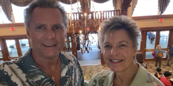 Two people smiling indoors with chandelier behind.