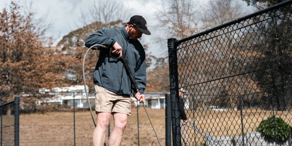 Man power washing a chain-link fence outdoors.
