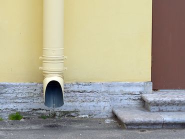 A yellow downspout on a pale yellow wall, with a concrete base and steps.