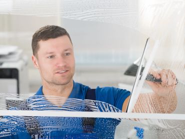 Smiling professional window cleaner in blue uniform using a squeegee to clean a glass surface.