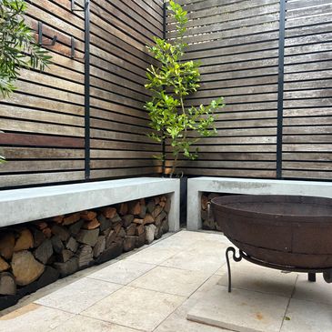 Modern outdoor seating area with stacked firewood and a metal fire pit.