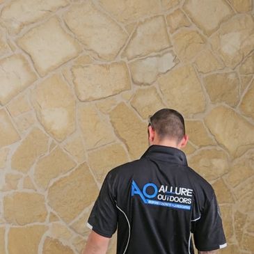 Man wearing a black shirt with 'Allure Outdoors' logo stands against a stone wall.
