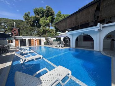 Sunny day by a serene pool with white lounge chairs and shaded tables.