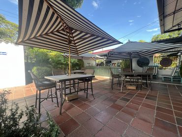 Outdoor patio with tables, chairs, and striped umbrellas under a clear sky.