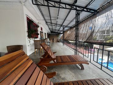 Covered patio with wooden lounge chairs overlooking a pool area.
