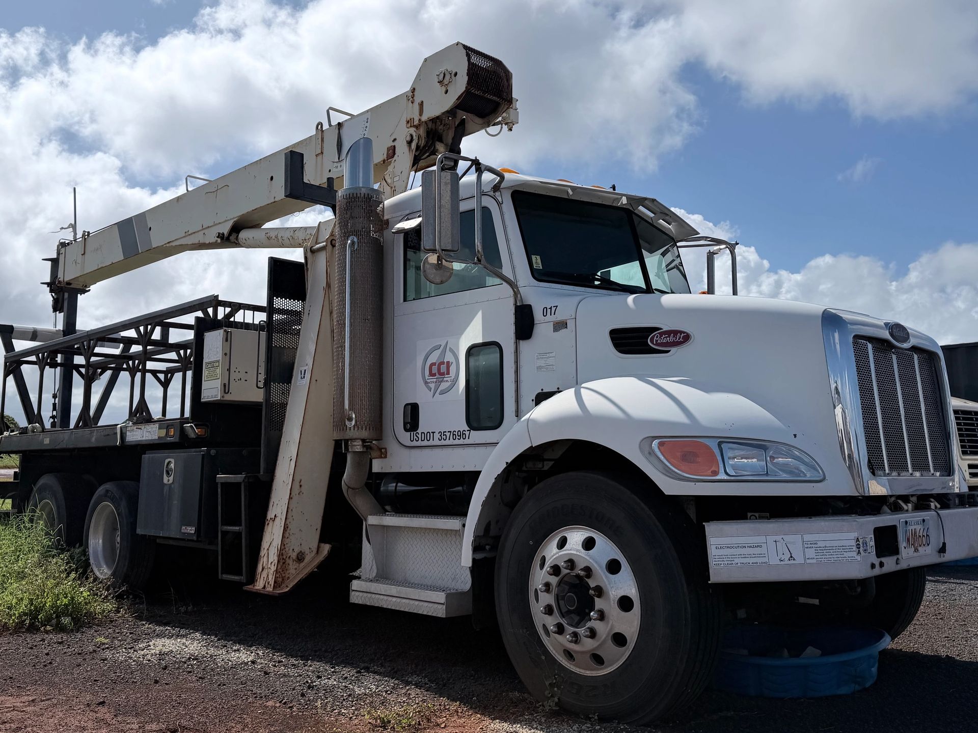 A white Peterbilt utility truck with an extended crane arm.