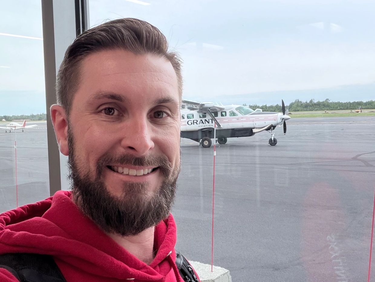 Smiling man in red hoodie at airport with small plane.