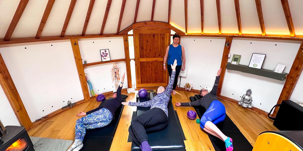 Three women practicing yoga with an instructor in a cozy wooden room.