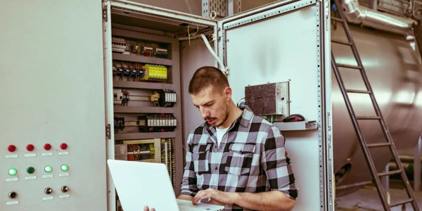 Technician working on an industrial control panel with a laptop.