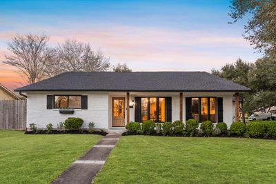 Single-story white brick house with black shutters and a well-kept lawn at sunset.