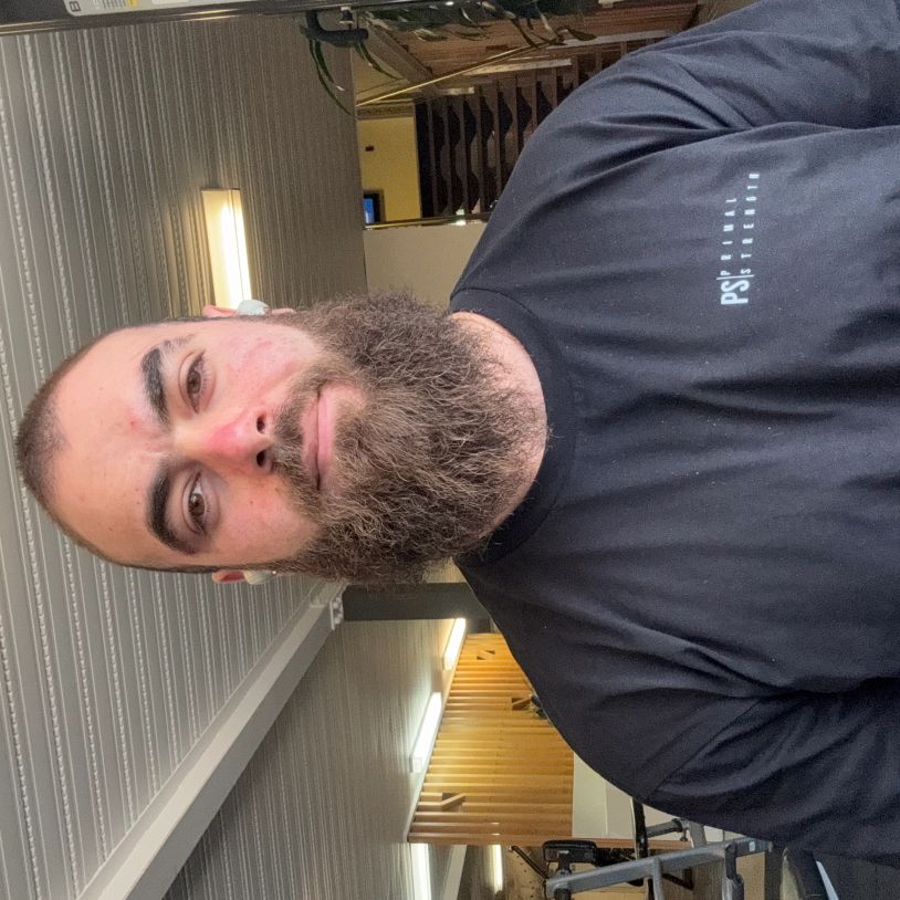 Bearded man wearing a black 'Primal Strength' t-shirt in a gym setting.
