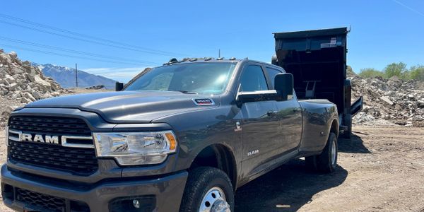 Gray RAM pickup truck parked near a dump trailer in a rocky area.