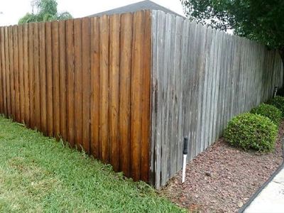 A wooden fence with one side stained brown and the other side weathered gray.