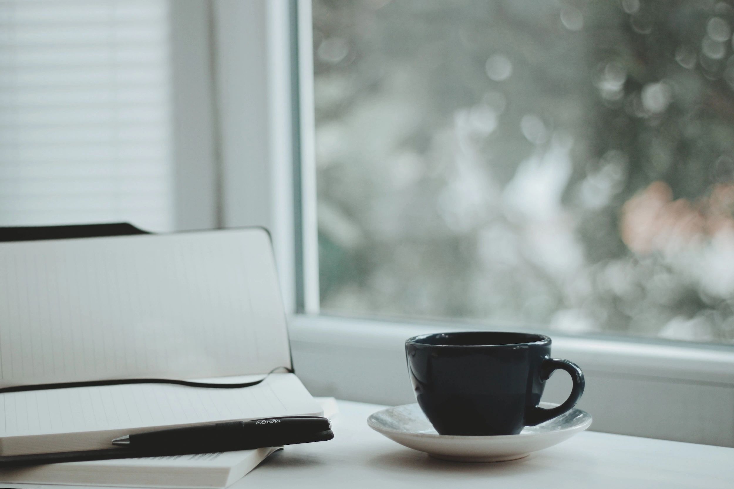 notebook, pen and coffee cup against a window