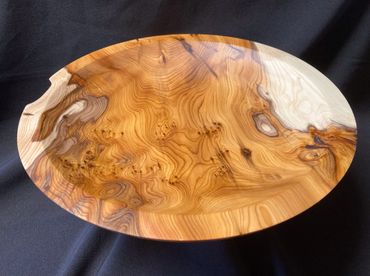 A polished wooden bowl with intricate natural grain patterns on a black cloth.