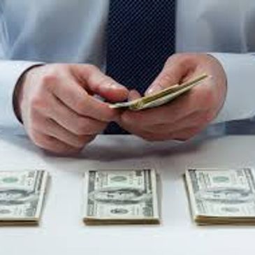 A picture of a man counting money on a table with stacks of 100.00