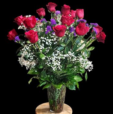 Elegant bouquet of red roses, purple statice, and white baby's breath in a glass vase.