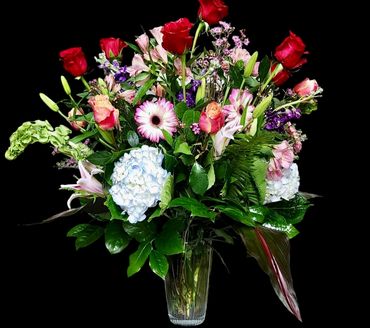 A vibrant bouquet of mixed flowers in a glass vase against a black background.