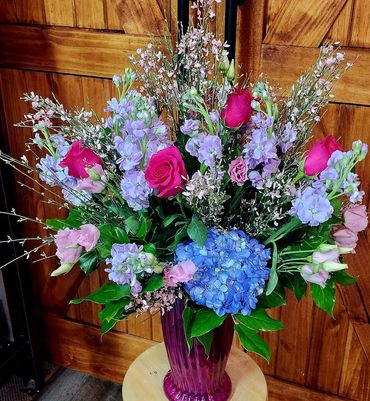 Colorful mixed flower bouquet in a purple vase on a wooden stool.