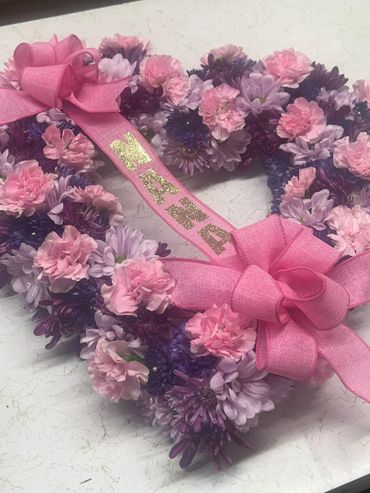 Heart-shaped wreath of pink and purple flowers with a pink ribbon.