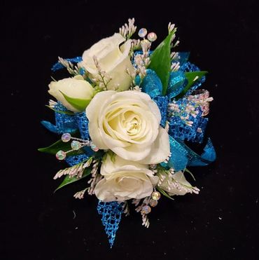 Elegant white rose corsage with blue ribbon and decorative accents.