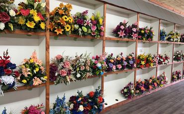 Colorful artificial flower arrangements displayed on wooden shelves.