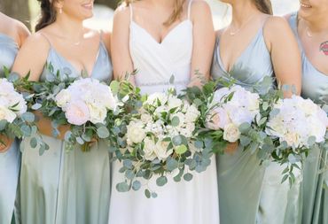 Bride and bridesmaids holding white and green floral bouquets in satin dresses.