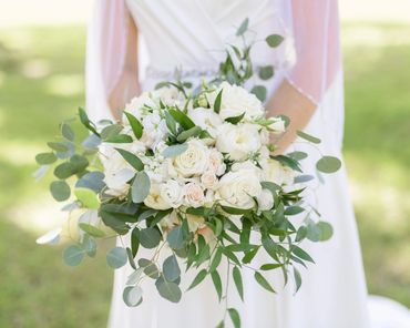 Bride holding a bouquet of white roses and greenery.