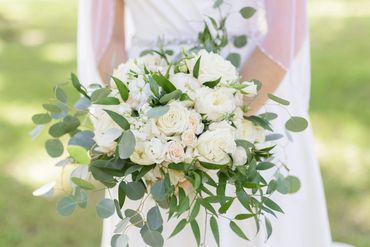 Bride holding a bouquet of white roses and greenery.
