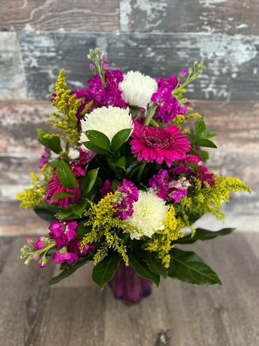 A vibrant bouquet with white, pink, and yellow flowers in a purple vase.