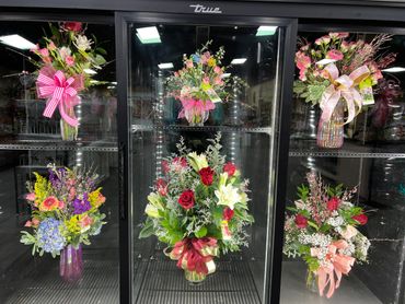 Colorful floral arrangements with ribbons inside a refrigerated display case.