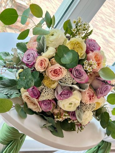 Elegant bouquet with pastel roses and greenery wrapped in white and green fabric.