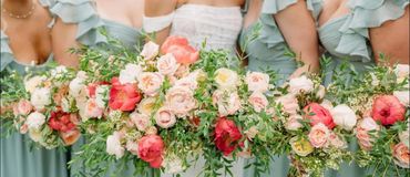 Bridesmaids in mint green dresses holding lush bouquets of pink, white, and coral flowers.
