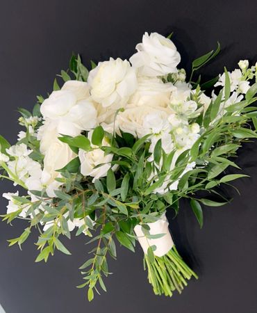 Elegant white floral bouquet with lush green foliage on black background.