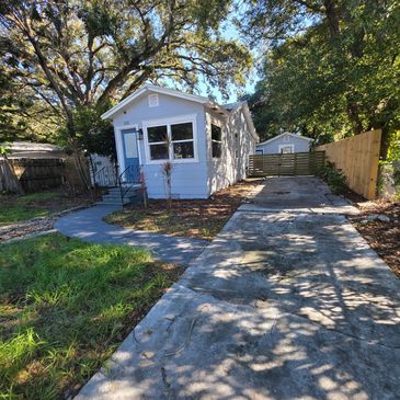 Small blue house with a driveway and trees.