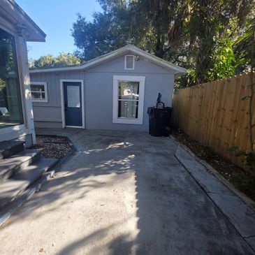 Small gray house with a fenced backyard and trash bins.