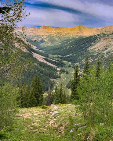 Looking into a valley with a creek running through it and mountains on all sides, and a very blue sk