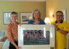 Three people holding a framed artwork in a cozy living room.