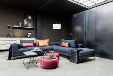 Hoekbank met losse rugkussens in een blauwe stof en cognac leder en strakke zwarte poten