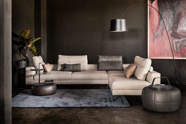 Beige design hoekzetel met speelse rugkussens, de bank in een beige stof en donker leder kussen