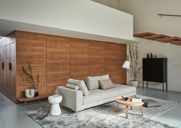 Strakke grijze zetel met losse rugkussens in modern interieur met noten hout