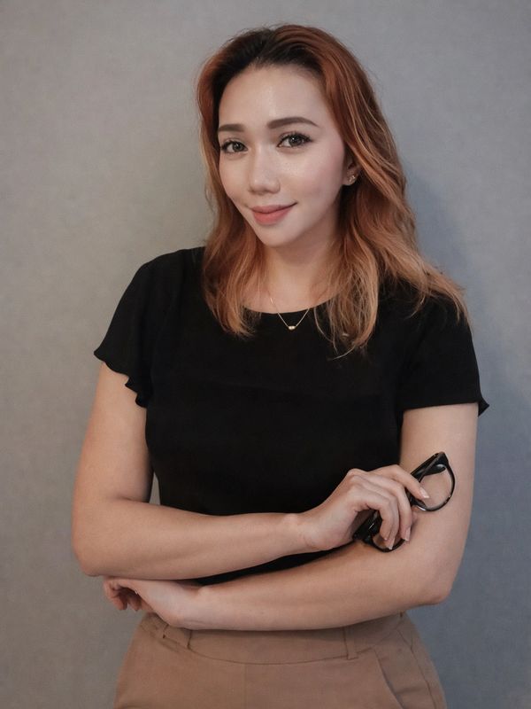 Woman with light brown hair wearing a black top, holding glasses and smiling.