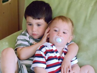 Two young boys sitting close on a green couch, one hugging the other.