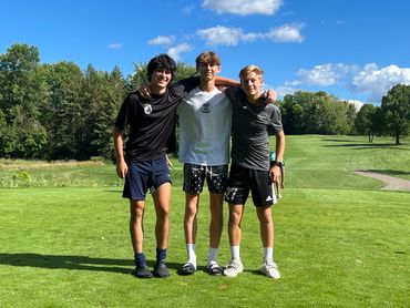 Three friends posing together on a sunny golf course with arms around each other.