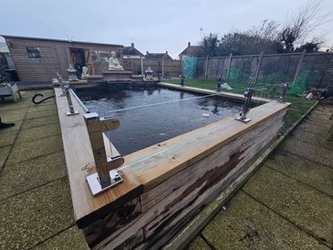 A large wooden hot tub outdoors with metal clamps on the edges.