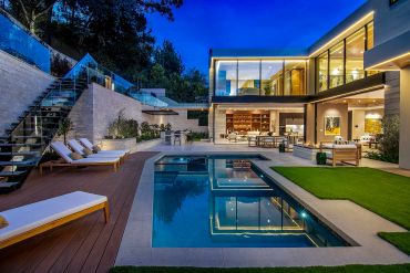 Luxurious modern house with illuminated pool and patio at dusk.