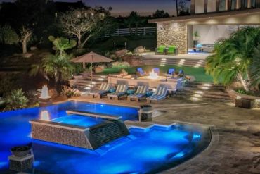 Luxury backyard pool area lit at night with fire pits.