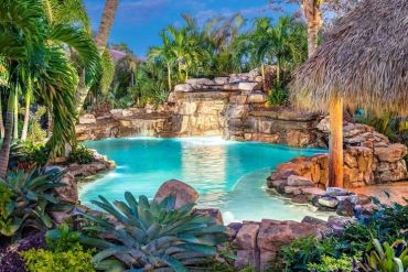 Tropical pool with waterfall and lush greenery.
