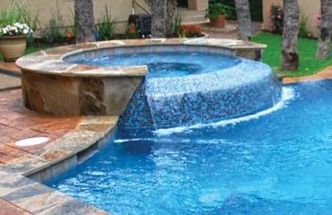 Outdoor pool with attached hot tub and waterfall feature.