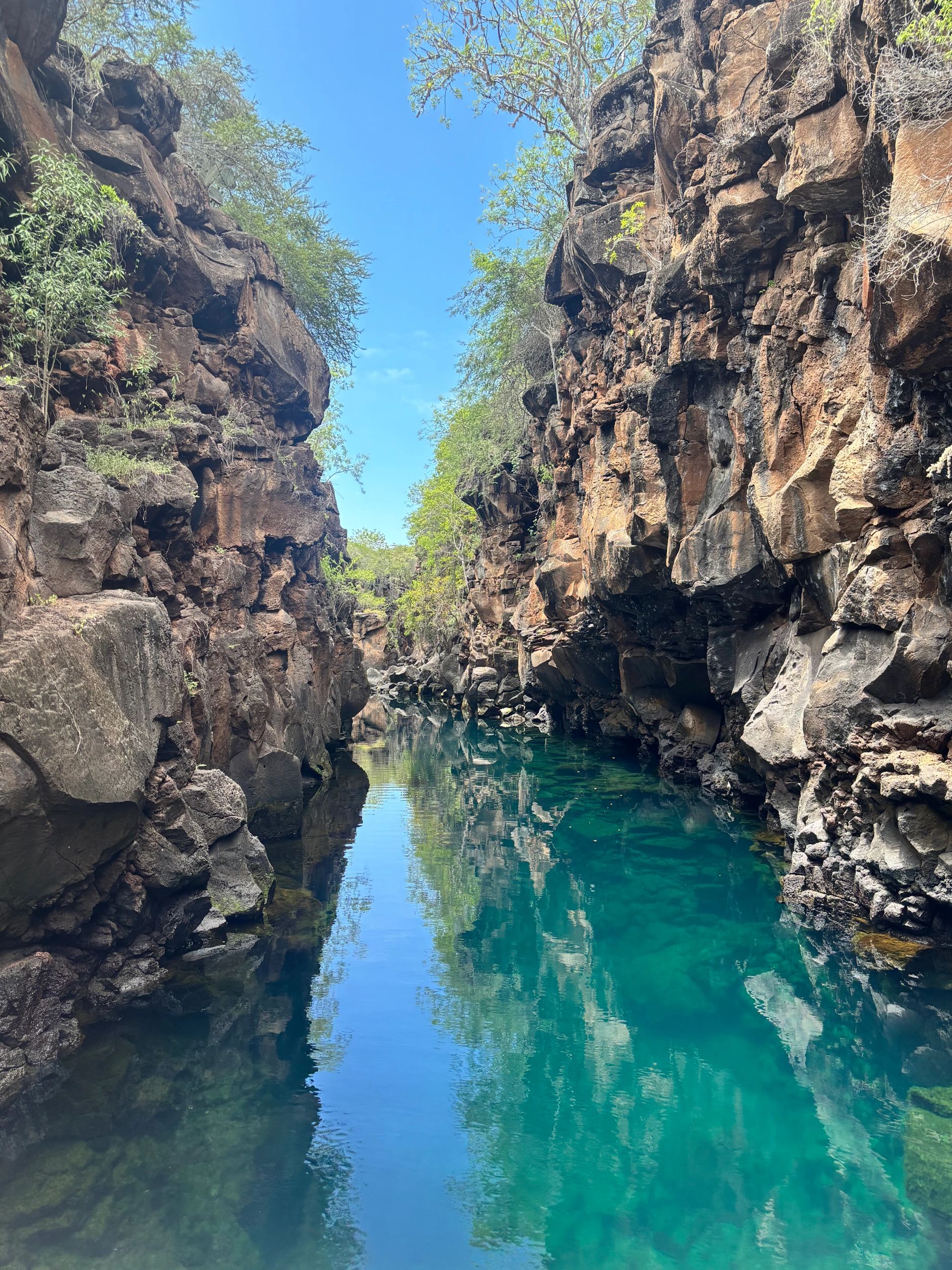 Clear blue water flows between rugged rocky cliffs under a bright sky.